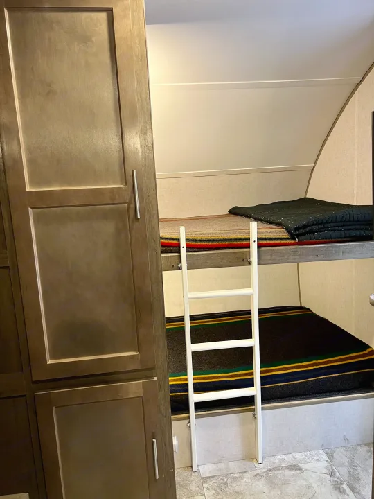 RV rental interior: bunk beds with colorful striped blankets, a white access ladder, and dark wood cabinets.. R-Pod Hood River Edition 2017