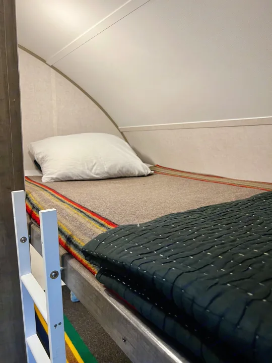 RV rental bunk bed: a cozy sleeping space with a white pillow, striped and dark quilted blankets. Perfect for travel.. R-Pod Hood River Edition 2017
