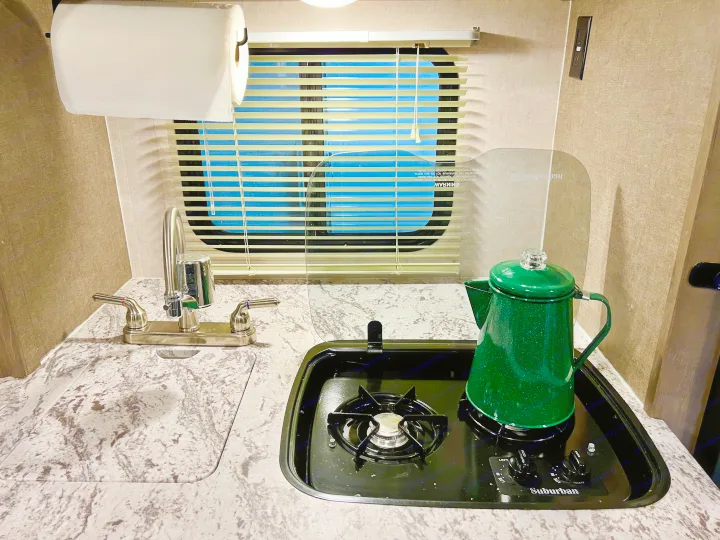 Inside an RV rental: a compact kitchen area featuring a sink, gas stove, and a green coffee percolator.. R-Pod Hood River Edition 2017