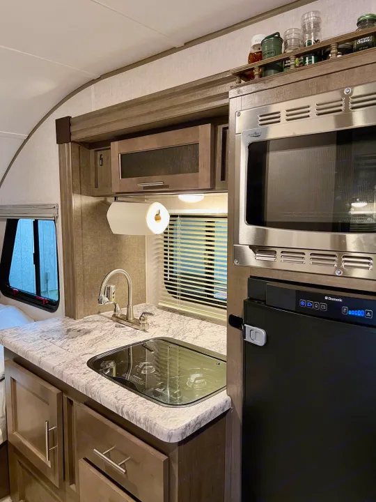 Functional kitchen in an RV rental, equipped with a High Pointe microwave, Dometic fridge, sink, & Suburban stovetop.. R-Pod Hood River Edition 2017