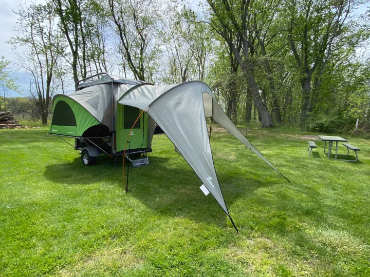 A SylvanSport GO pop-up camper with awning set up on grass. This unique trailer makes an excellent RV rental for camping.. SylvanSport GO 2022