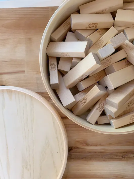 Wooden Jenga blocks are piled in a bowl, with its lid resting nearby on a wooden floor. Ideal for an RV rental game night.. Mercedes-Benz Sprinter 2016