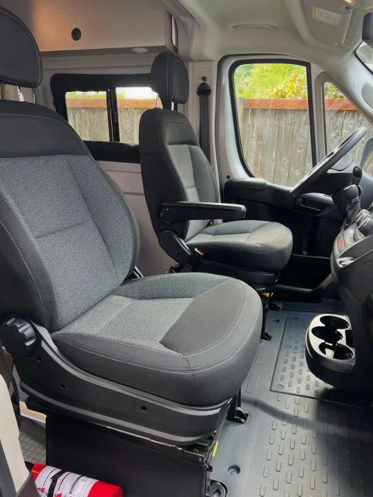 Clean RV rental cabin with swivel front seats, steering wheel, and floor mats. Note the fire extinguisher.. Winnebago Solis 2022