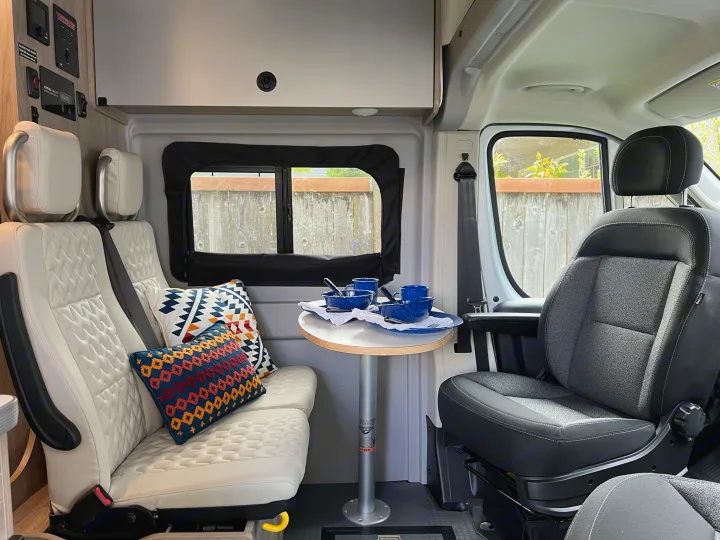 RV rental interior: cozy camper van dining area with white quilted seating, table, and controls.. Winnebago Solis 2022