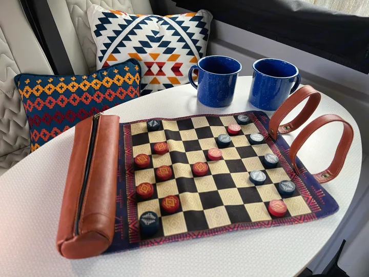 Cozy rv rental setup: a checkers game board, two blue enamel mugs, and patterned pillows. Ideal for relaxing travel.. Winnebago Solis 2022
