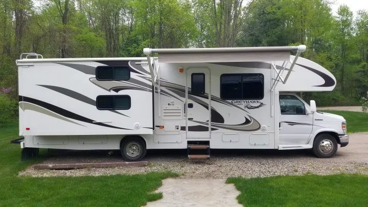 White Jayco Greyhawk RV with extended awning, parked on gravel near trees. A great option for your next rv rental adventure.. Jayco Greyhawk 2013