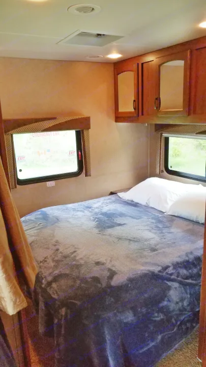 Cozy RV rental interior: a bedroom with a bed, two windows showing an emergency exit, and overhead wood cabinets.. Jayco Greyhawk 2013