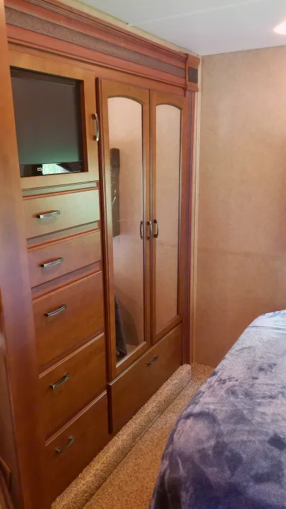 This RV rental interior showcases a bedroom with a built-in wooden cabinet, TV, mirrored wardrobe, dresser drawers, and a cozy bed.. Jayco Greyhawk 2013