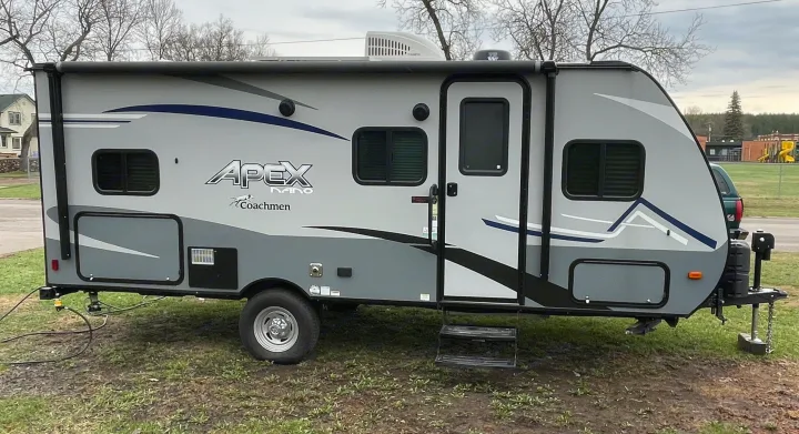 Modern grey and white Apex Nano travel trailer, a compact RV rental parked on grass, ideal for camping adventures.. Coachmen Apex Nano 2021