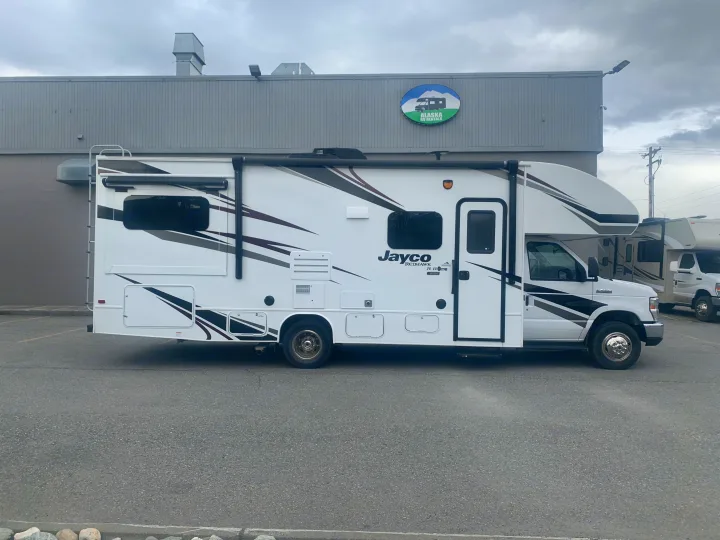 A white Jayco Redhawk Class C RV, an rv rental from Alaska RV Rentals, parked in front of a building.. Jayco Redhawk 2020