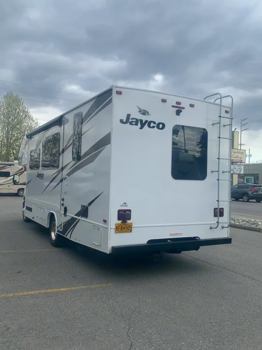 A white Jayco motorhome, an ideal RV rental for road trips, parked in a lot. Alaska plate KFA 505 visible.. Jayco Redhawk 2020