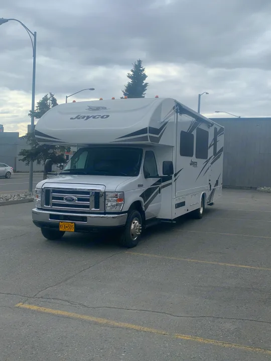 White Jayco RV rental parked in an Alaska lot under cloudy skies. Plate KFA 505.. Jayco Redhawk 2020