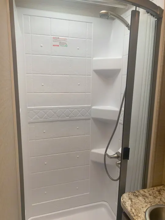 This compact, clean white RV shower, perfect for an RV rental, features built-in shelves and a detachable shower head.. Jayco Redhawk 2020