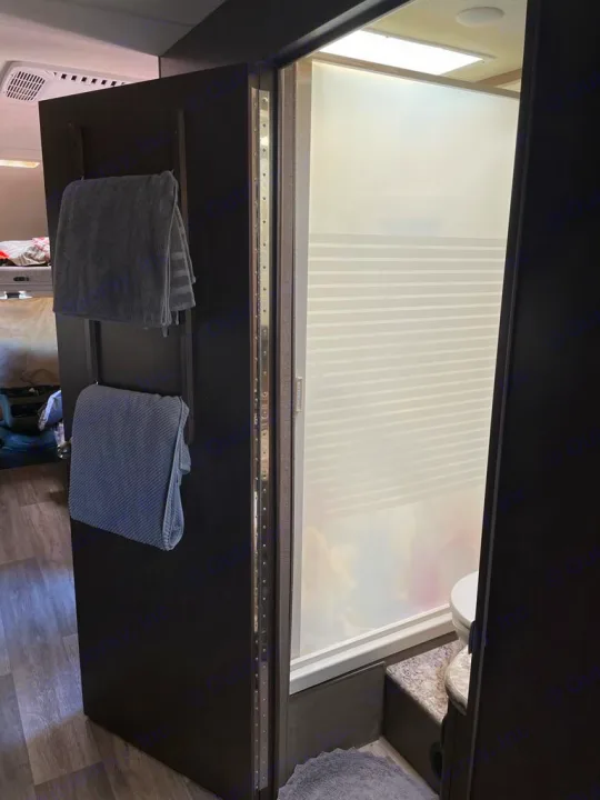 RV rental interior showing a compact bathroom with frosted shower door, toilet, & towel rack on a room divider.. Thor Motorcoach E450 Freedom Elite 2017