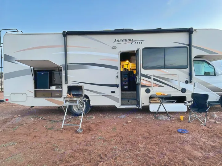 Freedom Elite rv rental set up for camping, with an outdoor kitchen, grill, and seating on red dirt.. Thor Motorcoach E450 Freedom Elite 2017
