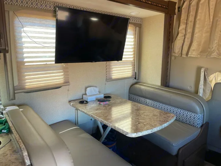 Spacious RV rental dinette with TV and comfortable seating, ideal for meals or relaxing during your camper travels.. Thor Motorcoach E450 Freedom Elite 2017