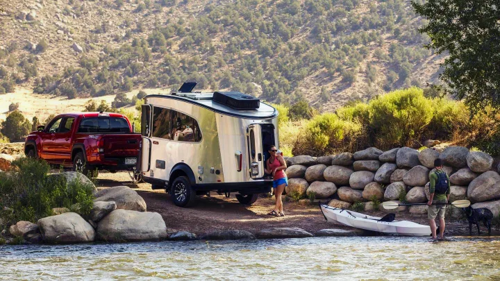 Rent an RV for outdoor fun! A truck pulls a sleek travel trailer by a river, with people and a kayak ready for adventure.. Airstream Base Camp 2023