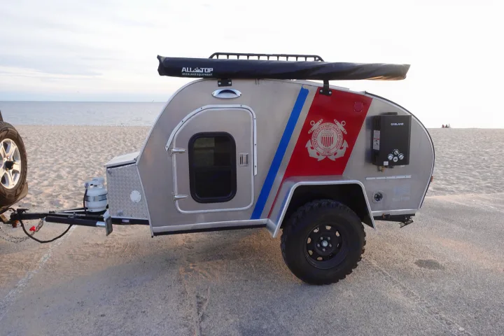 Unique USCG-themed overland trailer, available for RV rental, parked on a beach with ALLATOP gear & GASLAND heater.. Second Wind Freedom 2020