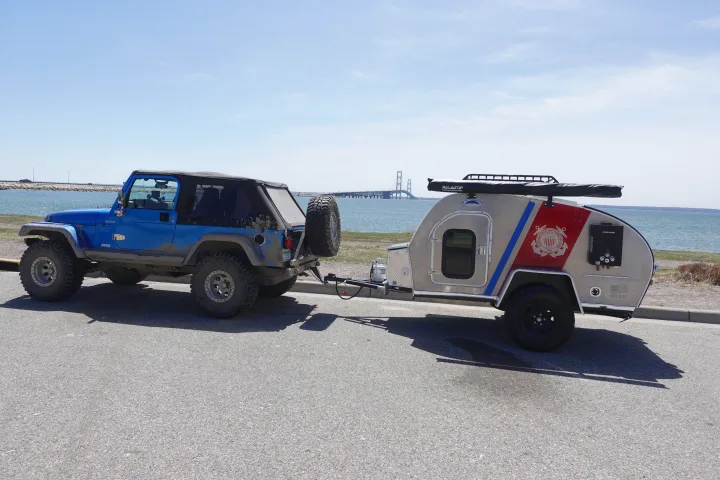 Overland RV rental: Blue Jeep towing a unique Coast Guard teardrop trailer by a scenic bridge.. Second Wind Freedom 2020