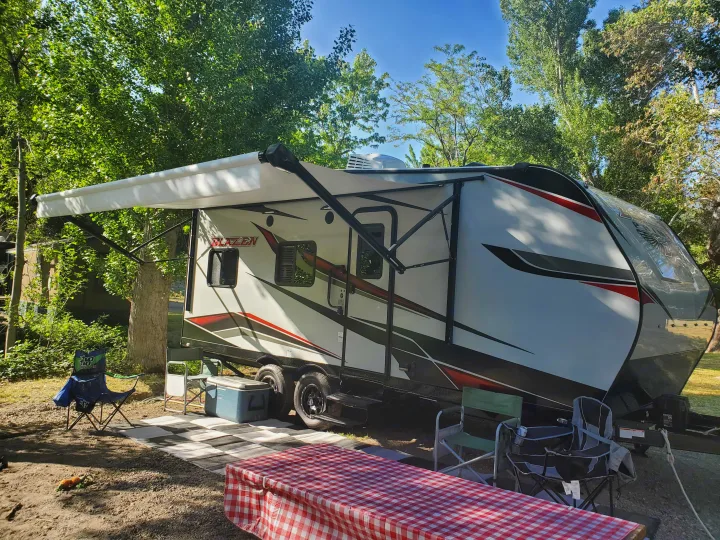 RV rental: Enjoy a spacious travel trailer with an extended awning set up at a serene campsite, perfect for outdoor living.. Pacific Coachworks Blaze'N 2022