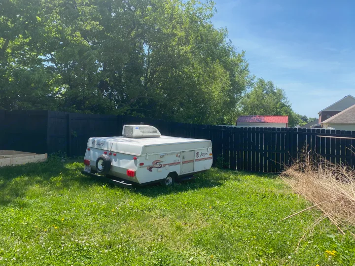 White Jayco pop-up camper with AC unit parked in a grassy backyard, surrounded by a black fence. Consider for RV rental.. Jayco Eagle 1996