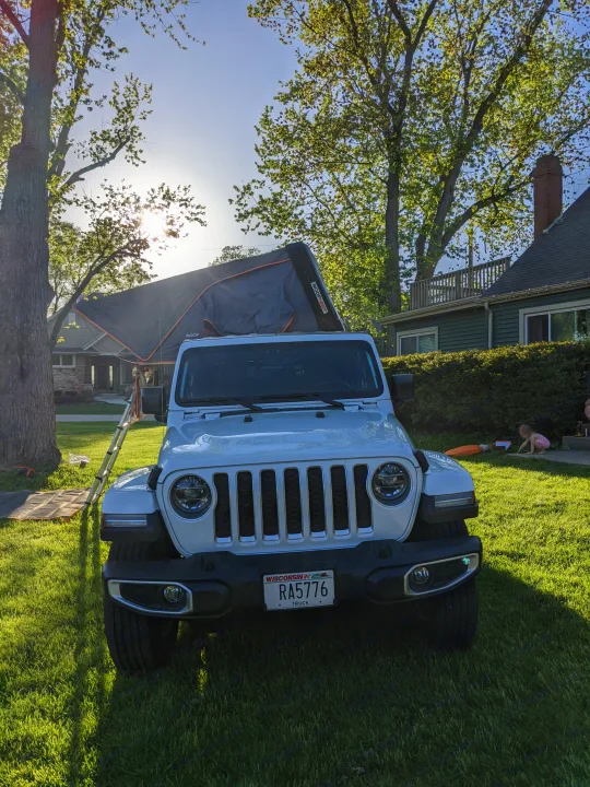 A white Jeep with an open rooftop tent sits on a sunny green lawn. Ready for adventure camping, offering an RV rental-like experience.. Jeep gladiator overland Jeep gladiator overland 2020