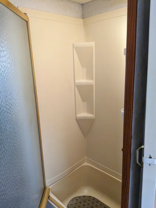 This RV rental features a compact beige corner shower unit with built-in shelves, textured glass door, and dark shower mat.. Holiday Rambler Atlantis 2003