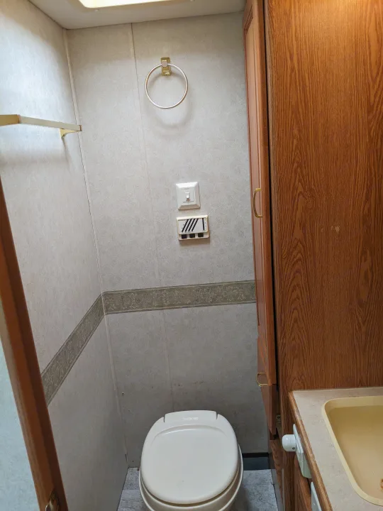RV rental bathroom with toilet, small sink, wood cabinets, towel ring, and light walls with decorative trim.. Holiday Rambler Atlantis 2003