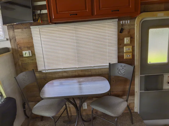 RV rental interior featuring a cozy dining area with coffee-themed chairs, table, window, and TV against wood walls.. Holiday Rambler Atlantis 2003