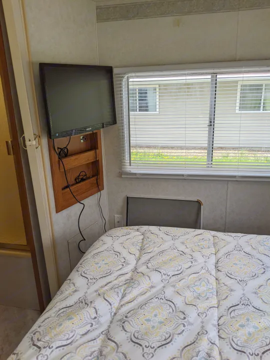 Cozy RV rental bedroom featuring a mounted TV, comfortable bed with patterned comforter, and window with blinds.. Holiday Rambler Atlantis 2003