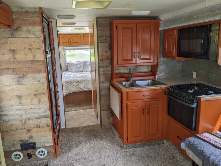 rv rental: Renovated RV interior featuring a kitchen with orange cabinets, wood-paneled walls, and a visible bedroom.. Holiday Rambler Atlantis 2003