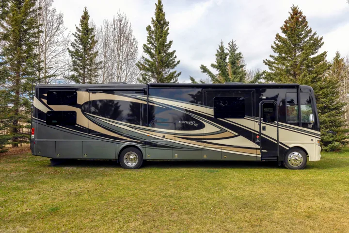 Large black & beige RV rental, a luxury motorhome with graphic designs, parked on green grass surrounded by trees.. Other Canyon Star 2020