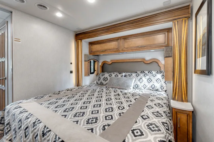 Cozy RV rental bedroom interior with a patterned bed, plush headboard, overhead cabinets, and modern lighting.. Other Canyon Star 2020