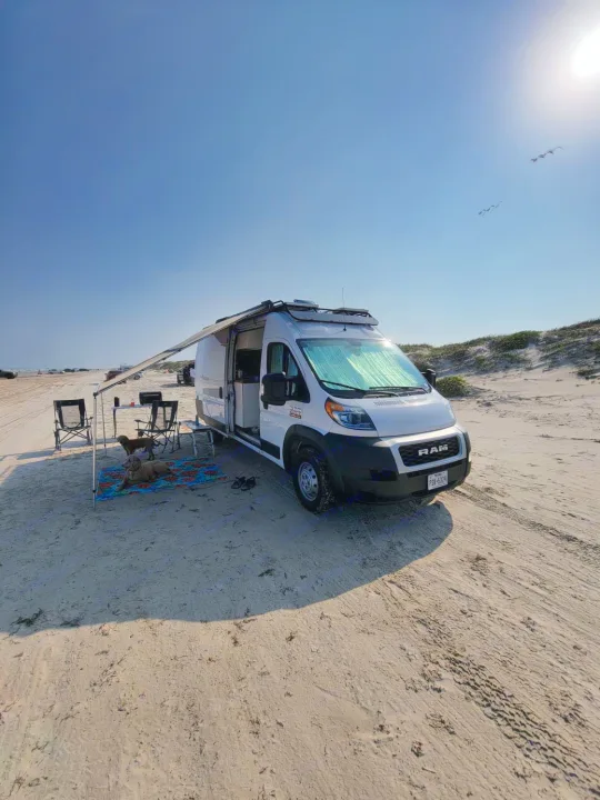 White RV rental enjoying beach camping, with dogs relaxing under the extended awning on sunny sand.. Other Other 2021