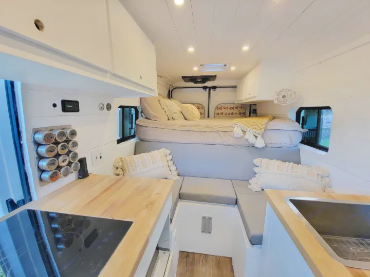 Inside a well-appointed rv rental van featuring a compact kitchen, comfortable elevated bed, and U-shaped lounge area.. Other Other 2021