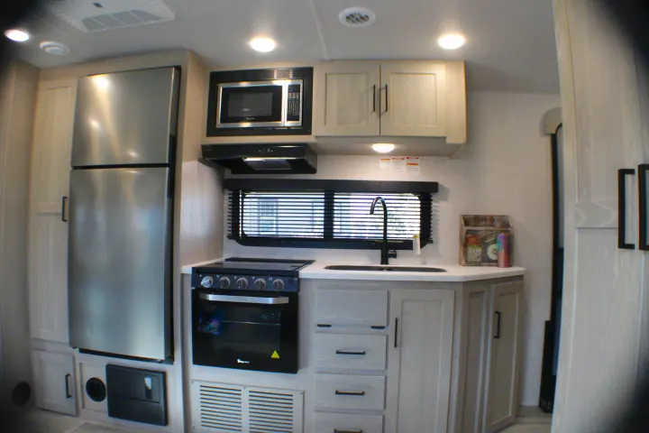 This RV rental kitchen offers essential amenities: a stainless fridge, microwave, oven, and sink in a light wood interior.. Forest River Rockwood Roo 2022