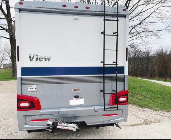 Rear view of a white and grey Winnebago View RV rental, featuring a ladder, camera, and tow hitch assembly.. Winnebago View 24J 2020