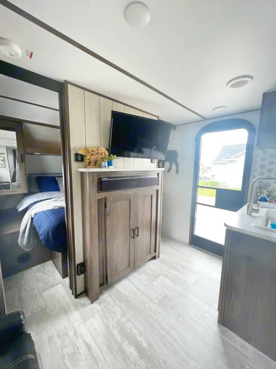 Modern RV rental interior showing bedroom, TV, and kitchen. Light wood-look flooring, compact living space.. Forest River Tracer LE 2020