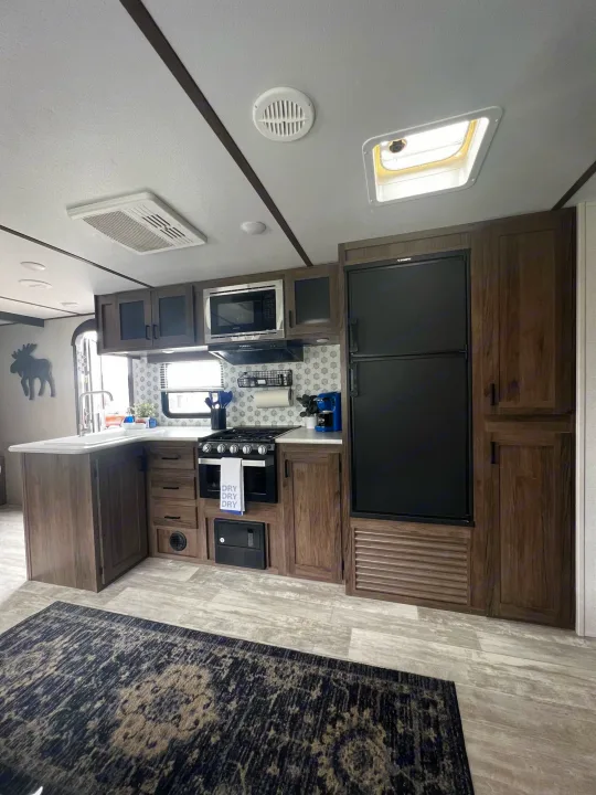 Modern RV rental kitchen interior with wood cabinets, black appliances, and light flooring. Perfect for your next adventure!. Forest River Tracer LE 2020