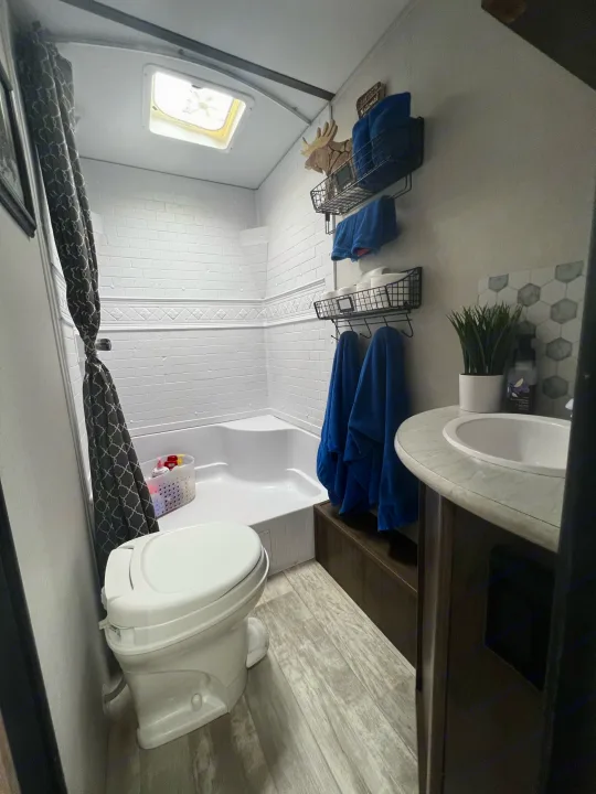 Inside a clean, compact RV rental bathroom with a toilet, shower, sink, and neat storage shelves.. Forest River Tracer LE 2020