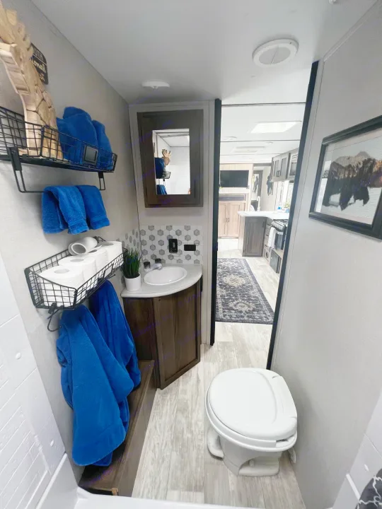 Cozy RV rental bathroom: sink, toilet, organized blue towels & TP storage. View of kitchen & living area beyond.. Forest River Tracer LE 2020