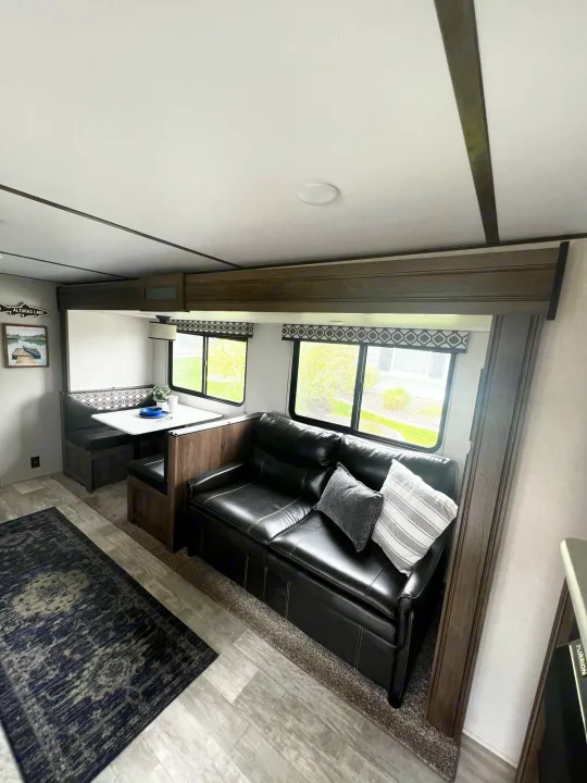 Cozy RV rental interior featuring a black leather sofa, dinette, and wood-look flooring for your travels.. Forest River Tracer LE 2020