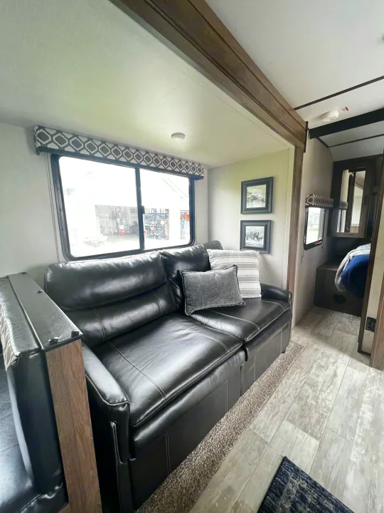 RV rental interior: A cozy living area features a black leather sofa, windows, and an entrance to the bedroom, offering comfortable travel.. Forest River Tracer LE 2020