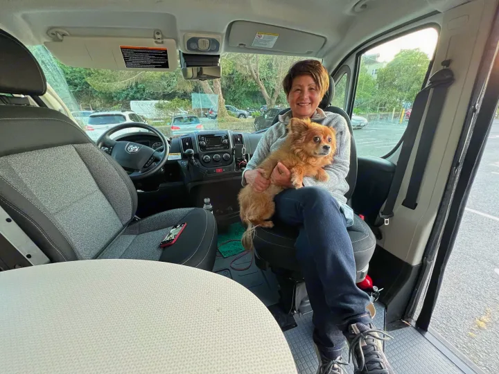 Happy woman and her fluffy dog smile inside a modern RV rental. A comfortable setup for pet-friendly road trip adventures.. Winnebago Winnebago Solis 59P 2022