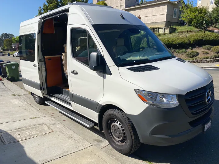 White Mercedes-Benz Sprinter camper van, ideal for rv rental, with its side door open showing a custom wood interior.. Vanworks Mercedes Benz Sprinter 2021