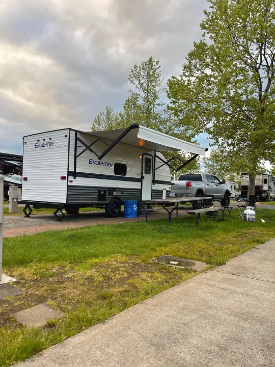 White Enlighten RV rental with awning extended, picnic table, and truck at a peaceful campground.. Gulf Stream Enlighten 18BH 2022