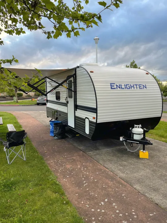 An 'Enlighten' rv rental, a white and gray travel trailer, is parked on a concrete pad at a campsite.. Gulf Stream Enlighten 18BH 2022