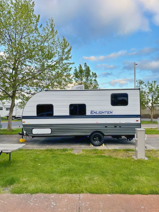 A clean travel trailer RV rental parked at a serene campsite under a partly cloudy sky.. Gulf Stream Enlighten 18BH 2022