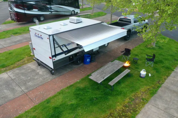 Experience outdoor leisure with this rv rental setup: a spacious travel trailer, truck, picnic table, and fire pit under the awning.. Gulf Stream Enlighten 18BH 2022