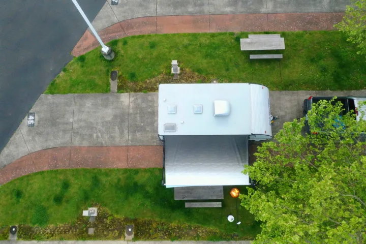 Overhead view of an RV rental campsite: a white travel trailer with awning, truck, picnic table, and glowing fire pit.. Gulf Stream Enlighten 18BH 2022